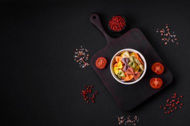 Koyu beton arka planda farklı renklerde çiğ farfalle makarna. İtalyan yemeği pişirmeye hazırlanıyor.