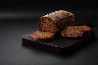 Koyu beton arka planda tahıl ve tohumlarla bir somun taze gevrek kahverengi ekmek.