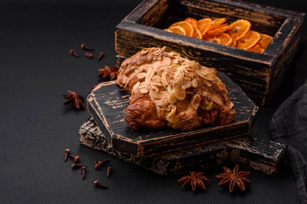 Fresh crispy croissant with almond chips and chocolate filling on a dark concrete background