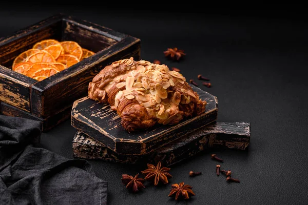 Fresh crispy croissant with almond chips and chocolate filling on a dark concrete background