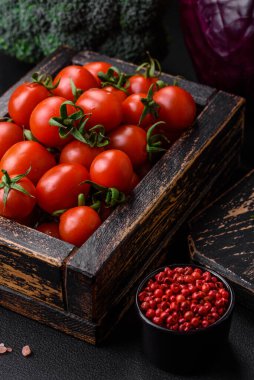 Koyu beton arka planda ahşap bir kutuda taze kırmızı kiraz domatesleri.