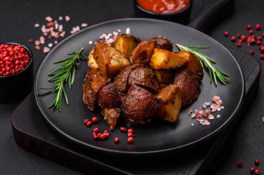 Biberiye ve baharatla kaplanmış, koyu beton arkaplanda pişirilmiş lezzetli patatesler.