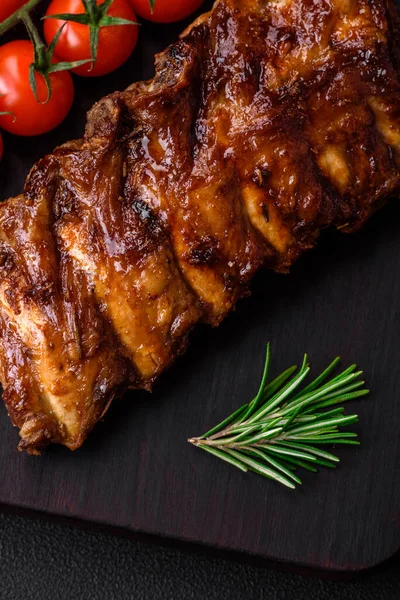 stock image Delicious grilled pork ribs with sauce, spices and herbs on a dark concrete background