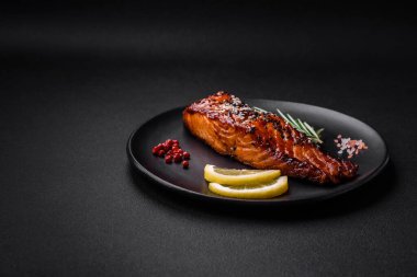 Delicious grilled red salmon fish with sauce, sesame seeds, spices and herbs on a dark concrete background clipart