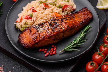 Lezzetli kırmızı somon balığı soslu ızgara ve susamlı pirinç, sebze, baharat ve çimento kaplı arka planda otlar.