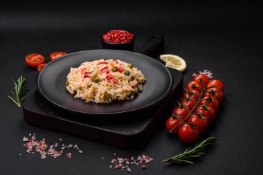 Lezzetli haşlanmış pirinç, sebzeli biber, bezelye ve kuşkonmaz fasulyesi, baharat ve otlu koyu beton arka planda.