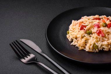 Lezzetli haşlanmış pirinç, sebzeli biber, bezelye ve kuşkonmaz fasulyesi, baharat ve otlu koyu beton arka planda.