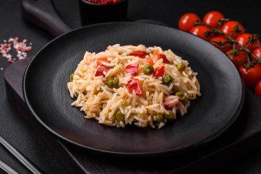 Lezzetli haşlanmış pirinç, sebzeli biber, bezelye ve kuşkonmaz fasulyesi, baharat ve otlu koyu beton arka planda.