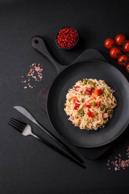 Lezzetli haşlanmış pirinç, sebzeli biber, bezelye ve kuşkonmaz fasulyesi, baharat ve otlu koyu beton arka planda.