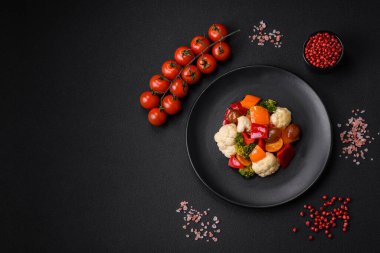 Taze vişneli domates salatası, tatlı biber, brokoli ve koyu beton arka planda tuz ve baharatlı karnabahar.