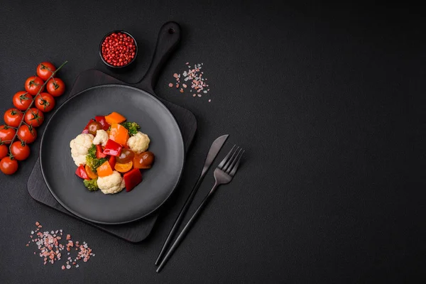 stock image Delicious salad of fresh cherry tomatoes, sweet peppers, broccoli and cauliflower with salt and spices on a dark concrete background