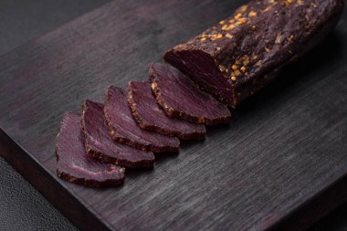 Lezzetli tütsülenmiş Ermeni basturması. Baharat ve otlarla birlikte koyu beton bir arka planda dilimlenmiş.