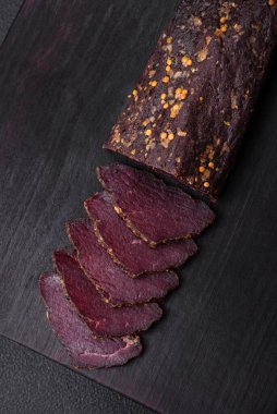 Lezzetli tütsülenmiş Ermeni basturması. Baharat ve otlarla birlikte koyu beton bir arka planda dilimlenmiş.