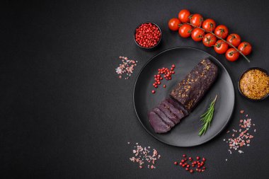 Lezzetli tütsülenmiş Ermeni basturması. Baharat ve otlarla birlikte koyu beton bir arka planda dilimlenmiş.