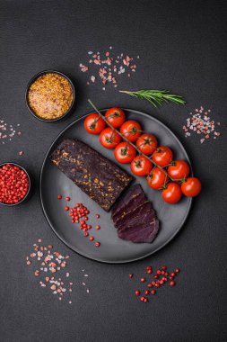 Lezzetli tütsülenmiş Ermeni basturması. Baharat ve otlarla birlikte koyu beton bir arka planda dilimlenmiş.