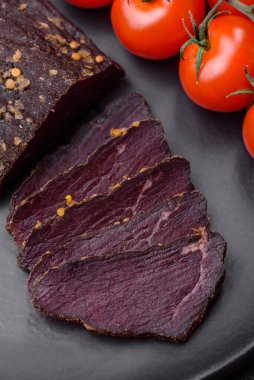 Lezzetli tütsülenmiş Ermeni basturması. Baharat ve otlarla birlikte koyu beton bir arka planda dilimlenmiş.