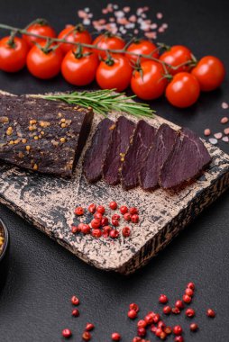 Lezzetli tütsülenmiş Ermeni basturması. Baharat ve otlarla birlikte koyu beton bir arka planda dilimlenmiş.