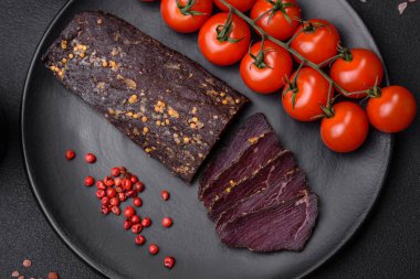 Lezzetli tütsülenmiş Ermeni basturması. Baharat ve otlarla birlikte koyu beton bir arka planda dilimlenmiş.