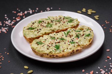 Avokado macunu, yumurta, krem peynir, tuz, baharat ve çimento kaplı bir masada ızgara tost.