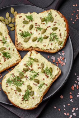 Avokado macunu, yumurta, krem peynir, tuz, baharat ve çimento kaplı bir masada ızgara tost.