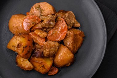 Lezzetli taze domuz etli yahni ya da koyu beton arka planda patates, havuç, baharat ve otlarla biftek.