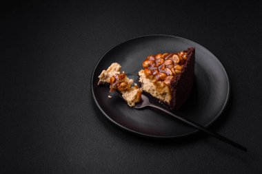 Lezzetli taze cheesecake keki ya da koyu beton arka planda seramik tabakta kremalı ve fındıklı snickers.
