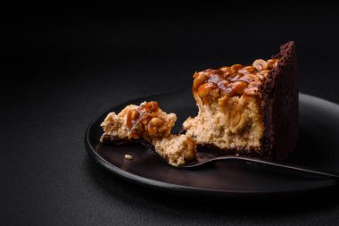 Lezzetli taze cheesecake keki ya da koyu beton arka planda seramik tabakta kremalı ve fındıklı snickers.