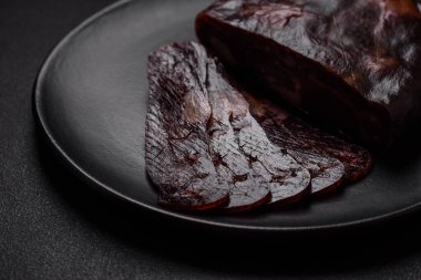 Lezzetli tütsülenmiş ya da kurutulmuş mahan atı eti sosisi baharat ve otlarla kaplı koyu beton arka planda.