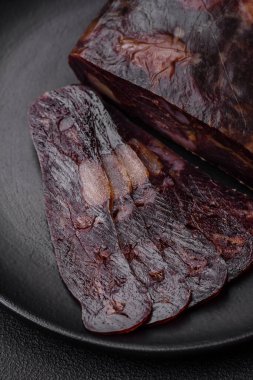 Lezzetli tütsülenmiş ya da kurutulmuş mahan atı eti sosisi baharat ve otlarla kaplı koyu beton arka planda.