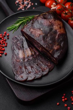 Lezzetli tütsülenmiş ya da kurutulmuş mahan atı eti sosisi baharat ve otlarla kaplı koyu beton arka planda.