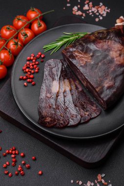 Lezzetli tütsülenmiş ya da kurutulmuş mahan atı eti sosisi baharat ve otlarla kaplı koyu beton arka planda.