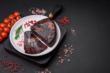 Lezzetli tütsülenmiş ya da kurutulmuş mahan atı eti sosisi baharat ve otlarla kaplı koyu beton arka planda.