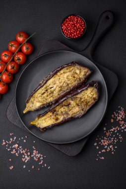 Tuz, baharat ve otlarla pişirilmiş, koyu beton arka planda iki parçaya ayrılmış lezzetli patlıcan.