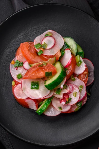 stock image Delicious vegan salad of fresh vegetables of tomatoes, cucumbers and radishes with salt and spices on a dark concrete background