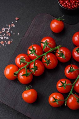 Lezzetli taze domatesler bir dal üzerinde baharatlar ve koyu beton bir arka planda otlar.