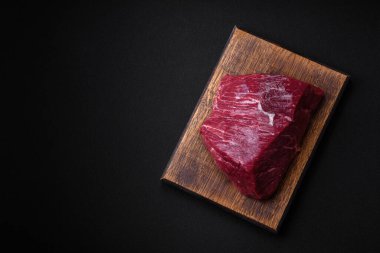 Tuzlu, baharatlı ve otlu taze çiğ et. Koyu beton bir arka planda tahta kesim tahtasının üzerinde.