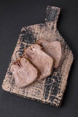 Lezzetli haşlanmış sığır dili. Koyu beton bir arka planda sebze ve baharatla dilimlenmiş.