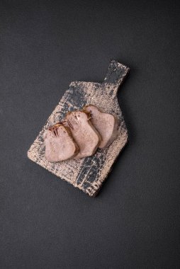 Lezzetli haşlanmış sığır dili. Koyu beton bir arka planda sebze ve baharatla dilimlenmiş.