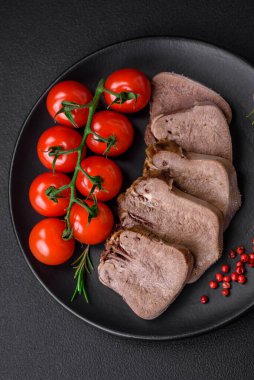 Lezzetli haşlanmış sığır dili. Koyu beton bir arka planda sebze ve baharatla dilimlenmiş.