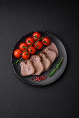 Lezzetli haşlanmış sığır dili. Koyu beton bir arka planda sebze ve baharatla dilimlenmiş.