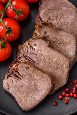 Lezzetli haşlanmış sığır dili. Koyu beton bir arka planda sebze ve baharatla dilimlenmiş.