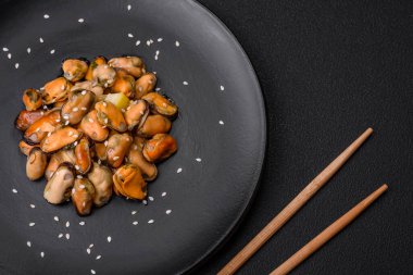 Çimento arka planında seramik tabakta baharat ve otlarla marine edilmiş lezzetli midyeler.