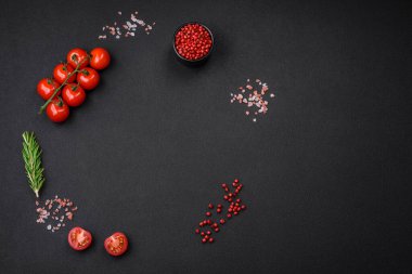 Boş siyah dokuma masası, ince bir dal üzerinde kiraz domatesleri, baharatlar, tuz ve bitkiler. Evde yemek pişirmek için gerekli malzemeler