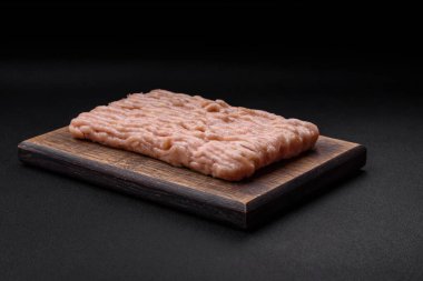 Ahşap kesme tahtasının üzerinde tuz, baharat ve otlarla kaplı taze doğranmış tavuk.