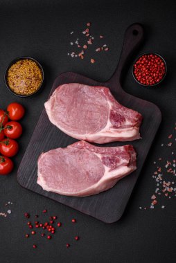 Kemikte çiğ domuz eti ya da tuz, baharat ve otlarla dilimlenmiş koyu beton arka planda kesilmiş kaburga.