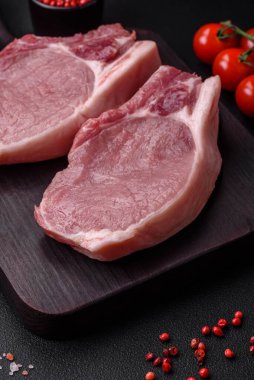 Kemikte çiğ domuz eti ya da tuz, baharat ve otlarla dilimlenmiş koyu beton arka planda kesilmiş kaburga.