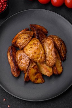 Lezzetli ızgara patates dilimleri, sarımsak, baharat ve otlar koyu beton arka planda.