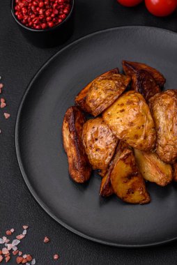 Lezzetli ızgara patates dilimleri, sarımsak, baharat ve otlar koyu beton arka planda.