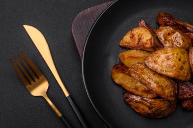 Lezzetli ızgara patates dilimleri, sarımsak, baharat ve otlar koyu beton arka planda.