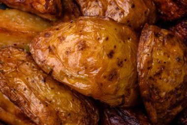 Lezzetli ızgara patates dilimleri, sarımsak, baharat ve otlar koyu beton arka planda.